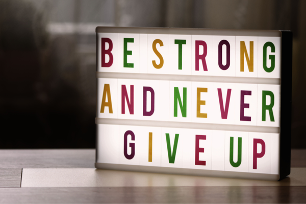 Leuchtbox mit der Aufschrift „Be strong and never give up“ auf einem Tisch.